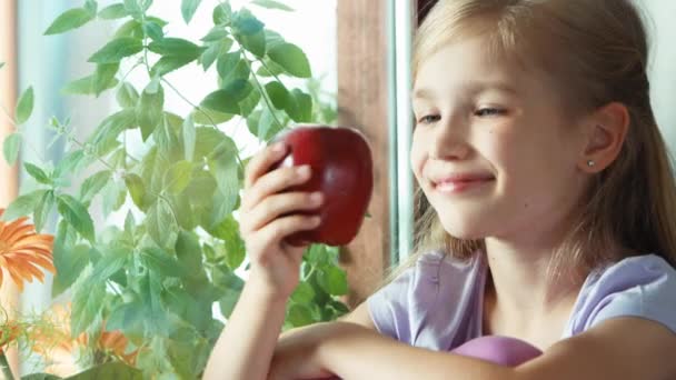 Ragazza che mostra mela rossa. Bambino seduto su un davanzale vicino alla finestra. Il bambino annuisce. Zoomare — Video Stock