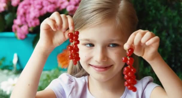 Rapariga a mostrar um monte de groselhas vermelhas. Brincos de groselha. Criança sentada na mesa no jardim — Vídeo de Stock