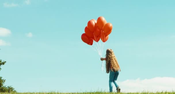 Chica con globos rojos contra el cielo agitando la mano y riéndose de la cámara — Vídeo de stock