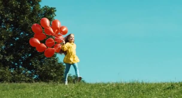Meisje is in gele regenjas uitgevoerd met rode ballonnen tegen de hemel — Stockvideo