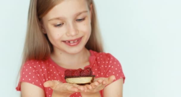 Meisje holding en snuiven een cake met frambozen. Meisje met mooi blond haar op een witte achtergrond. Closeup — Stockvideo