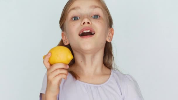 Girl biting a lemon and a curving face. Child laughing at the camera. Closeup — Stockvideo