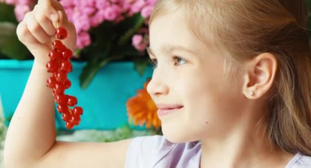 Girl eating very tasty sweet red currant and looking at camera. Child sitting on the table in the garden. Big eyes — Αρχείο Βίντεο