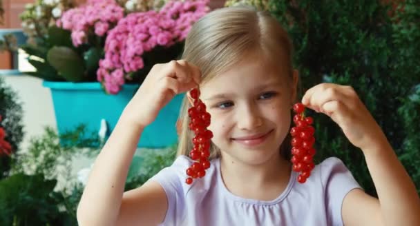 Сережки з смородини. Дівчина показує купу червоної смородини. Дитина сидить на столі в саду — стокове відео