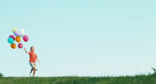 Het kind spinnen met ballonnen en draait op het gras. Meisje gekleed in korte broek en T-shirt — Stockvideo