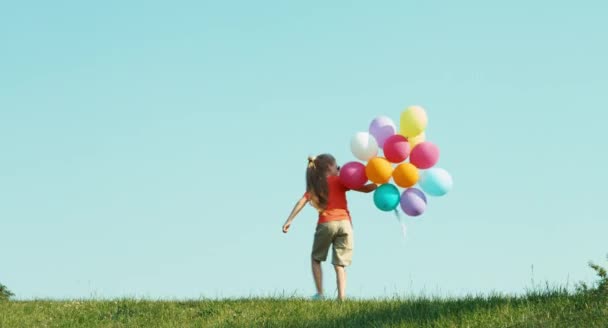 Chica vestida con pantalones cortos y camiseta sosteniendo globos y saludando con la mano — Vídeo de stock