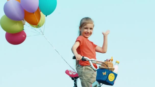 Дівчина махає рукою до камери. Вона тримає велосипед з повітряними кульками. У кошику є хліб і молоко — стокове відео