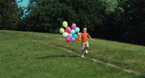 Chica alegre corriendo con globos en el parque — Vídeo de stock