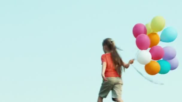 Девушка, одетая в шорты и футболку, держит воздушные шары и машет рукой — стоковое видео