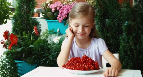 La chica tiene un plato grande de grosella roja. Niño sentado en la mesa en el jardín. Pulgar hacia arriba. Ok. — Vídeo de stock