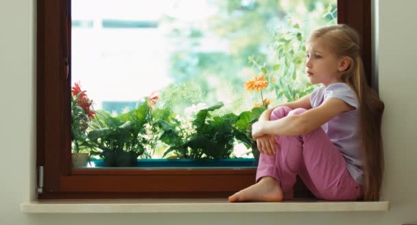 Chica triste sentado en un alféizar de la ventana y mirando por la ventana — Vídeos de Stock