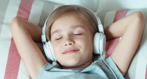 Closeup portrait girl child listening music in headphones and lying on the bed and resting — Stockvideo