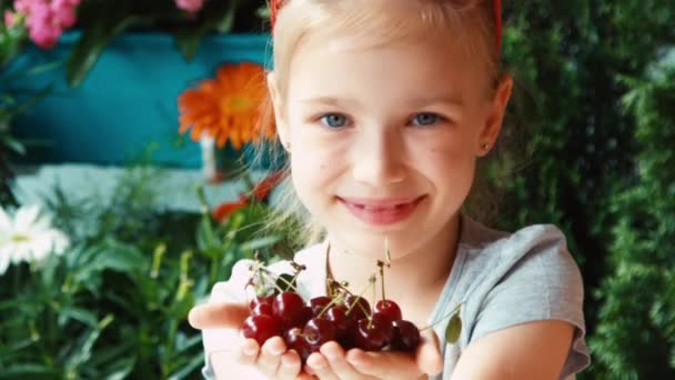 Dziewczyna portret zbliżenie wąchania jagody. Dziecko trzyma garść wiśni i podziwia jagody i patrząc na kamery — Wideo stockowe