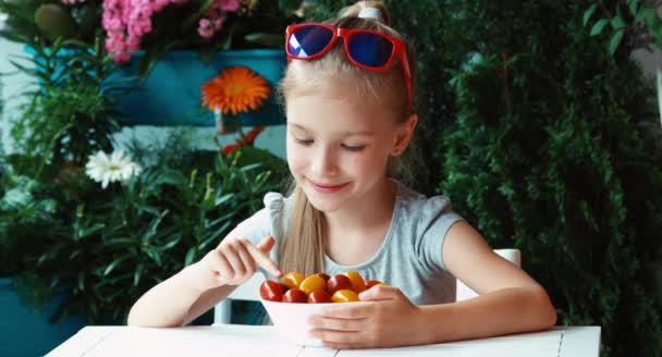 Дівчина їсть вишневий помідор і посміхається на камеру. Палець вгору. гаразд — стокове відео