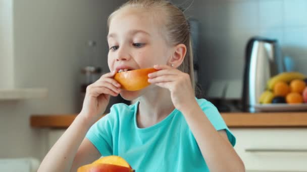 Chica comiendo mango. Niño sentado en la mesa de la cocina y mirando a la cámara. Pulgar hacia arriba. De acuerdo. Ampliación — Vídeos de Stock