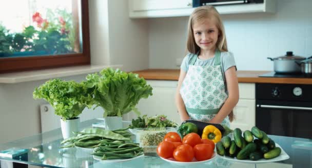 若い女の子のシェフは野菜を推進しています。台所のテーブルの近くに立って、カメラで笑顔の女の子 — ストック動画