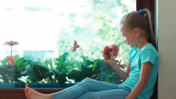 Girl eating peach. Girl nods her head at camera. Child sitting on the windowsill and looking out the window. Zooming — Stock Video