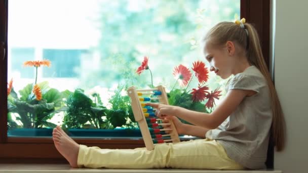 Lány tanulás-hoz számolás abacus, és ülve az ablakpárkányra. Kicsinyítés/nagyítás — Stock videók