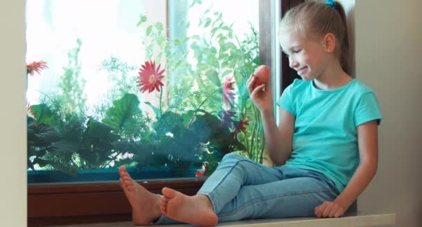 Portrait fille manger pêche et assis sur le rebord de la fenêtre et regarder par la fenêtre et la caméra — Video