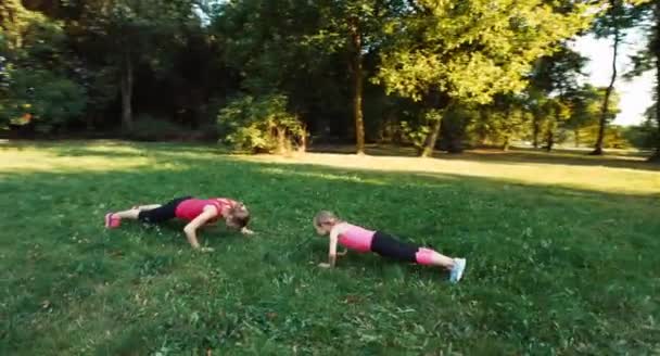 Сім'я спортсменів, мати і дочка займаються фітнесом в парку. Камера літає навколо 4 — стокове відео