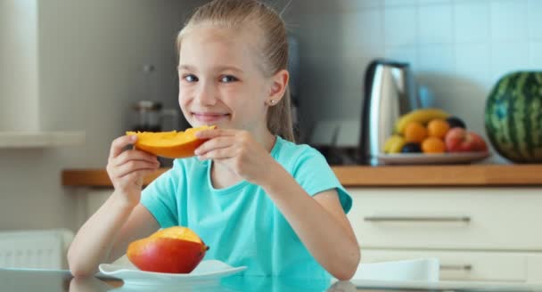 Meisje eten mango. Kind zit aan de tafel in de keuken — Stockvideo