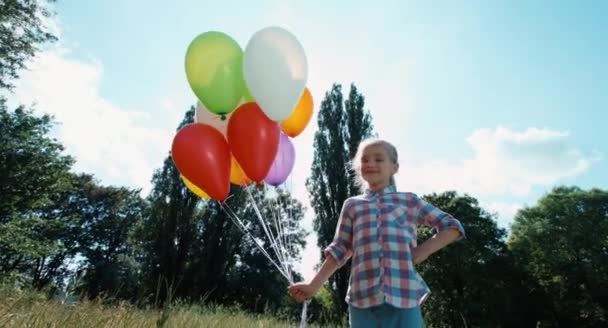 Chica sosteniendo globos contra el sol. Niño con globos en el parque. Lente llamarada — Vídeo de stock