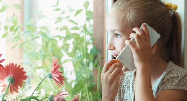 Kind meisje wortelen eten en praten op een mobiele telefoon — Stockvideo
