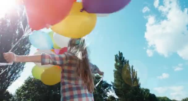 Menina 6-8 anos de idade girando com balões contra o céu na luz do sol — Vídeo de Stock