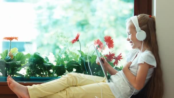 Muchacha de retrato usando tableta pc contra la flor. Chica escuchando música en los auriculares. Pulgar hacia arriba. De acuerdo. Ampliación — Vídeo de stock