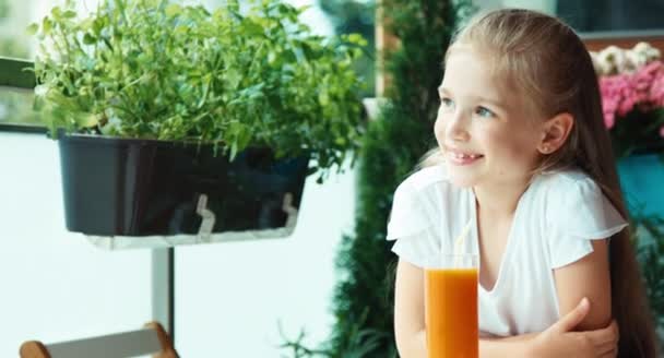 Retrato menina beber suco contra a flor e sorrindo para a câmera — Vídeo de Stock