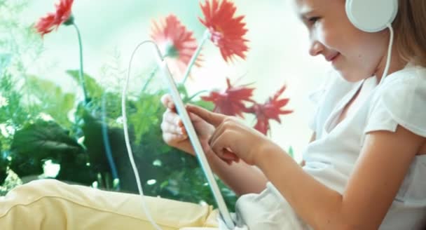 Zbliżenie portret dziewczyny przy użyciu komputera typu tablet przed kwiat. Dziewczyna słuchanie muzyki na słuchawkach. Tak ręka. Ok — Wideo stockowe