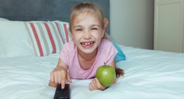 Flicka byta Tv ligger på sängen. Barn holding grön äpple — Stockvideo