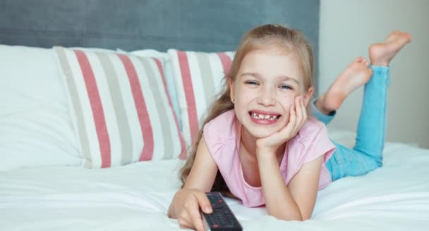 Una chica sonriente viendo televisión. Niña acostada en la cama. Niño impactado TV — Vídeos de Stock