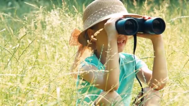 Retrato riendo joven naturalista a través de prismáticos observando la vida silvestre. Niño sentado en la hierba alta. Ampliación — Vídeos de Stock