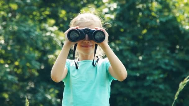 Girl looking through binoculars at camera and waving hand and laughing — Stock Video