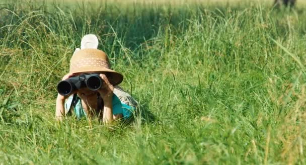 Jovem explorador naturalista com binóculos assistindo a vida selvagem. Criança deitada na grama — Vídeo de Stock