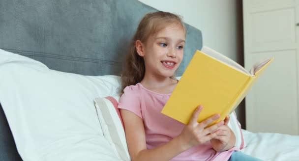 Девушка читает книгу и улыбается в камеру — стоковое видео