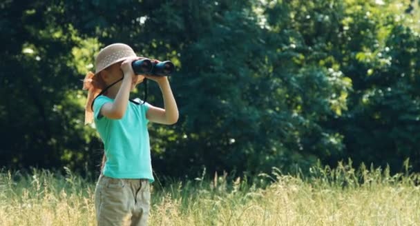 Kind permanent in het gras, en houden van de verrekijker. Meisje kijken naar dieren. Camera kijken en lachen — Stockvideo