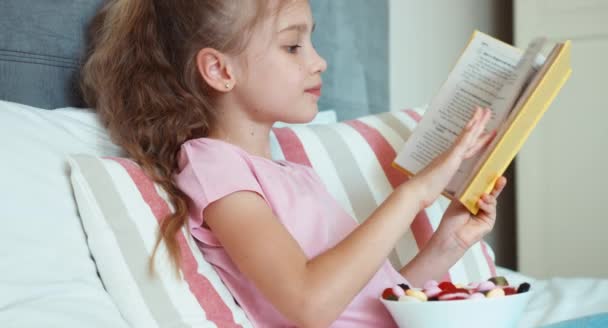 Zbliżenie portret dziewczyna dziecko czytając książkę i jedzenie słodycze — Wideo stockowe