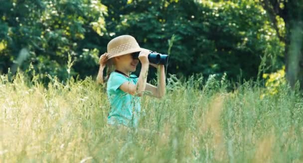 Fille regardant à travers les jumelles à distance. L'enfant allume la caméra et sourit — Video