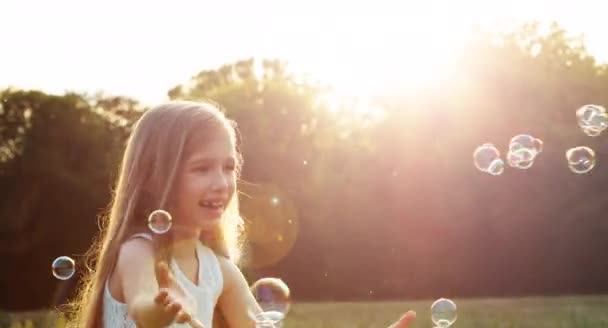 Κορίτσι πιάνει σαπούνι φυσαλίδες στο φως του ήλιου και του φακού φωτοβολίδα. Ευτυχισμένο παιδί που γελάει — Αρχείο Βίντεο