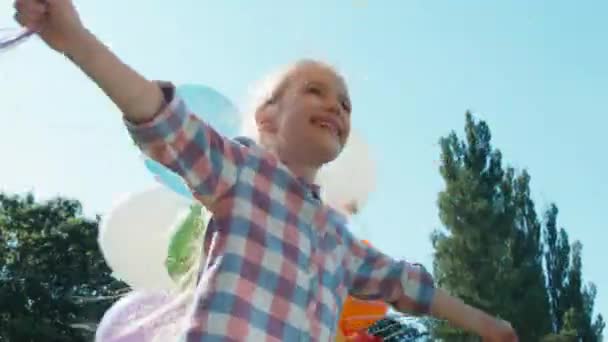 Närbild porträtt av lekfulla flicka spinning på kameran med ballonger i parken och titta på kameran — Stockvideo