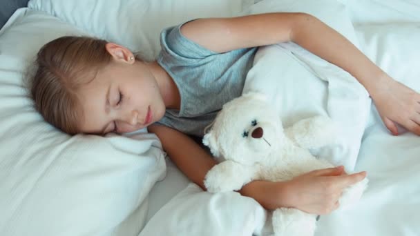 Menina retrato 6-8 anos dormindo com ursinho de pelúcia em uma cama e abraçando brinquedo. Vista superior. Zumbido — Vídeo de Stock