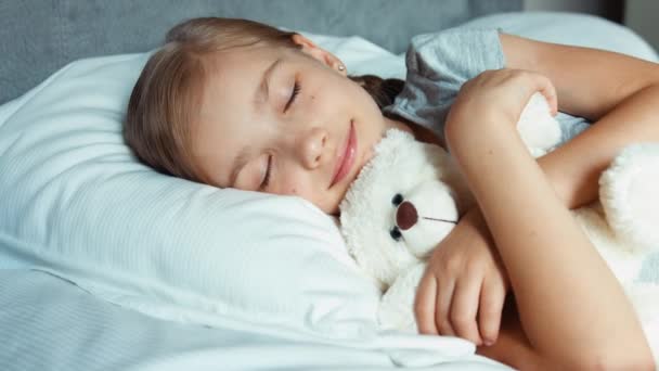 Девушка спит в постели с плюшевым мишкой и улыбается. Zooming — стоковое видео