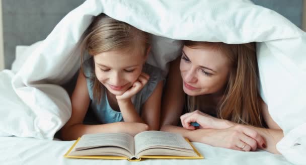 Primo piano ritratto famiglia madre e figlia lettura libro sotto la coperta e ridere della macchina fotografica — Video Stock