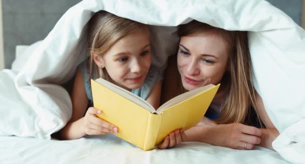 Primer plano retrato familia madre e hija lectura libro bajo la manta y riendo — Vídeo de stock