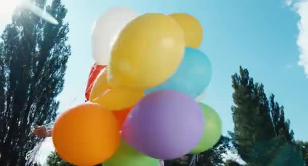 Девушка крутится с воздушными шарами и смотрит на камеру в парке — стоковое видео