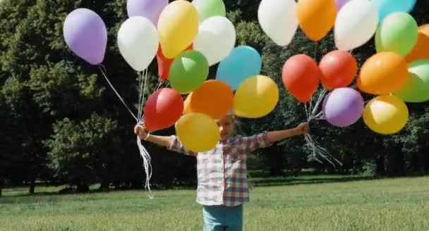 Портрет смеющейся девушки, у которой много воздушных шаров. Дети кружатся в парке — стоковое видео