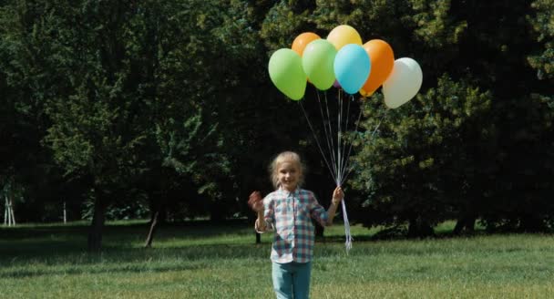 Mädchen winkt in die Kamera. lachendes Mädchen, das viele Luftballons vor der Kamera laufen hat — Stockvideo