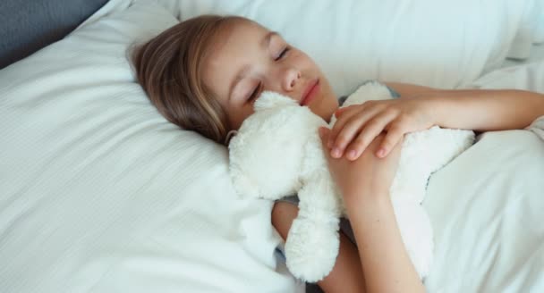 Το παιδί κορίτσι παίζει με αρκουδάκι και αγκαλιάζει το παιχνίδι σε ένα κρεβάτι. Το Top view — Αρχείο Βίντεο